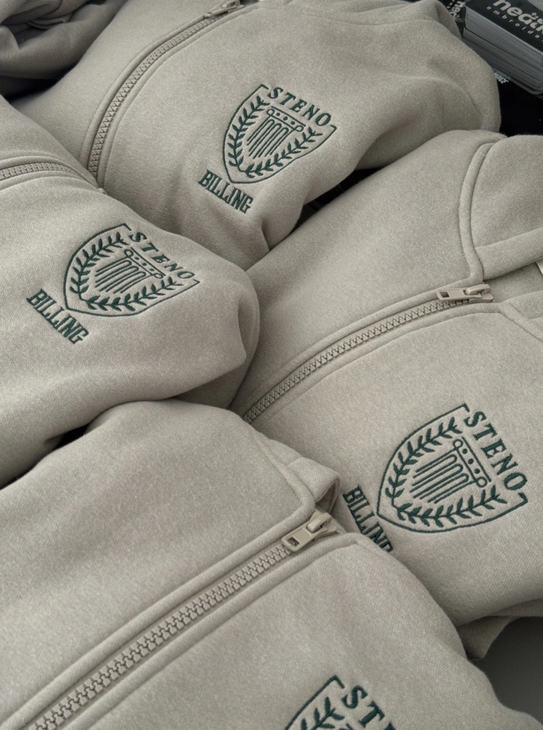 Sage zip-up sweatshirts embroidered in dark green with the Steno crest and BILLING